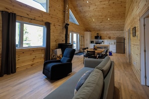 A wooden cabin interior with a sofa, armchair, dining table, and kitchen area.