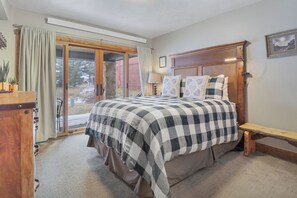 A bedroom with a large bed, a wooden headboard, and a sliding glass door leading to a patio. - Ski in Ski Out w/ Shared hot tub and Amazing Views (Copper Mountain)