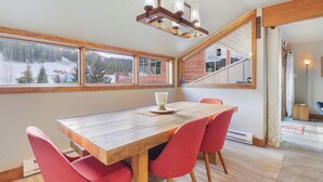 En matplats med ett träbord och röda stolar, stora fönster med utsikt över ett snötäckt landskap och en trappa som leder till en annan våning.