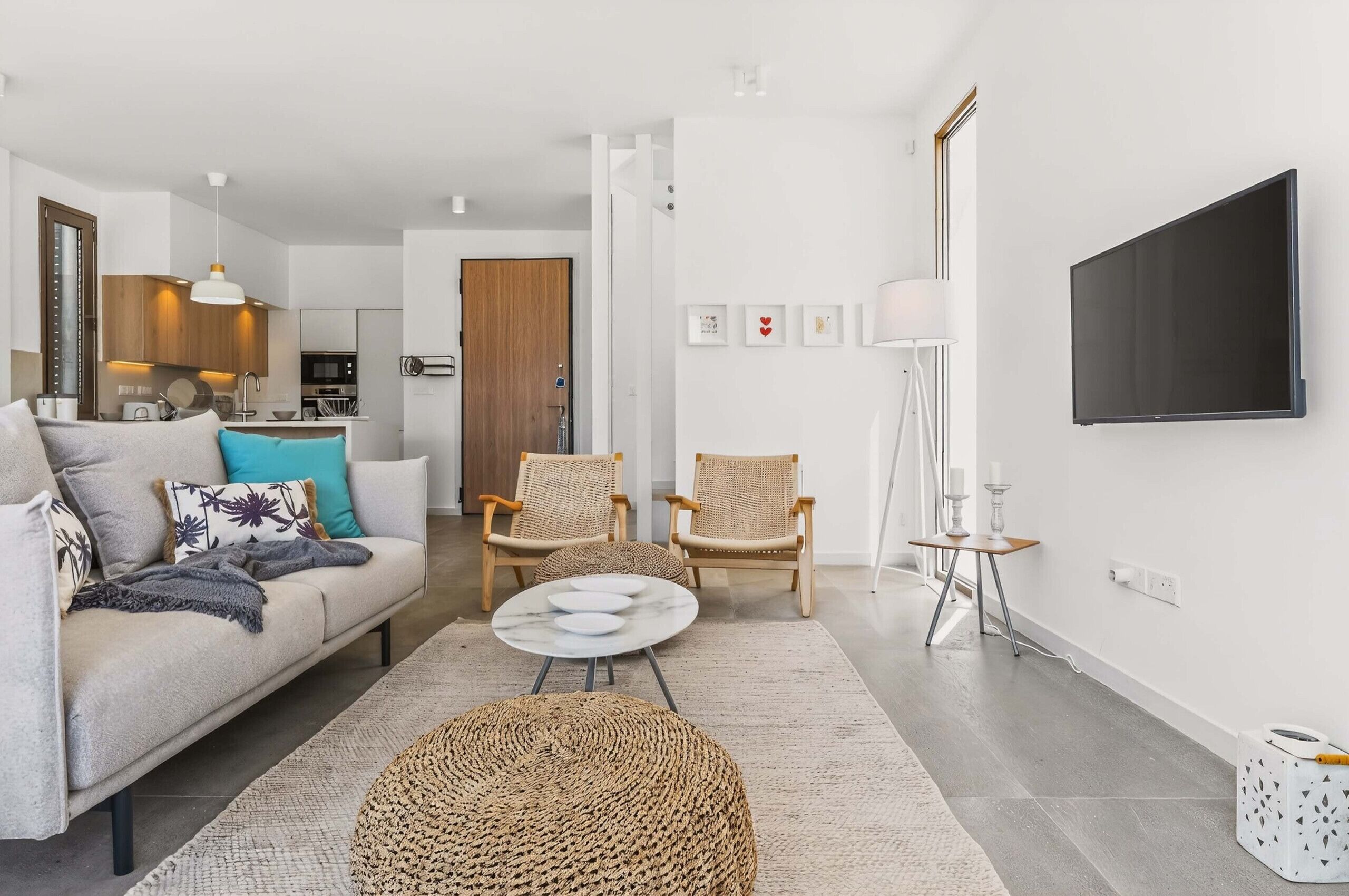 A modern living room with a sofa, two wicker chairs, a coffee table, and a flat-screen TV mounted on the wall.