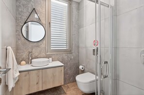 Une salle de bain moderne avec un grand miroir rond, un lavabo, des toilettes et une douche à parois de verre.