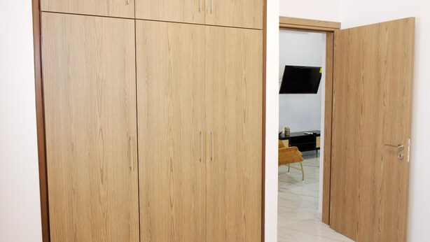 Una habitación con un armario de madera, un televisor de pantalla plana montado en la pared y una mesita con una silla.