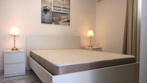 Un dormitorio con una cama, dos mesitas de noche con lámparas, una mesilla auxiliar y una pared con tres cuadros.