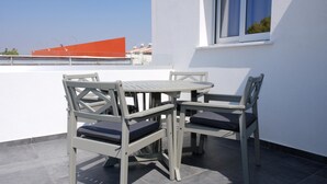 Un patio con una mesa redonda y cuatro sillas, una ventana que ofrece vista a un edificio con techo naranja, y una pared blanca.