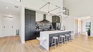Una cucina moderna con una grande isola, mobili scuri e un soffitto alto con travi a vista.