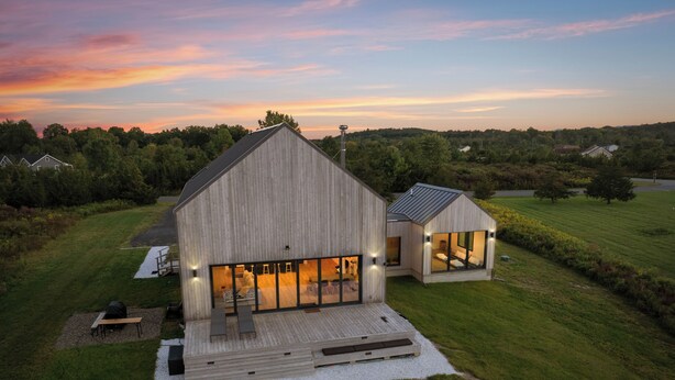 Una moderna casa in legno con un'ampia terrazza e una struttura più piccola ad essa collegata, immersa in un paesaggio erboso.