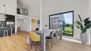 Una cucina moderna con un frigorifero in acciaio inox, un tavolo da pranzo in legno con sedie e un'ampia finestra che si affaccia su una casa e sul verde.