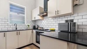 A modern kitchen with white cabinets, a black countertop, a stainless steel range hood, a built-in oven, and a microwave. - Art Haus Sea Point (Cape Town)