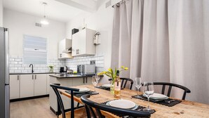 A modern kitchen with white cabinets, a wooden dining table, and black chairs. - Art Haus Sea Point (Cape Town)
