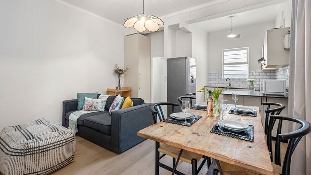 A modern kitchen with white cabinets, a stainless steel refrigerator, and a window with blinds. - Art Haus Sea Point (Cape Town)