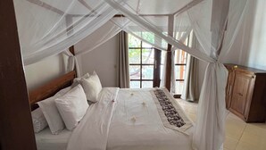 Ein Schlafzimmer mit einem Himmelsbett, einem Holzkopfteil und Blick ins Freie durch ein Fenster.