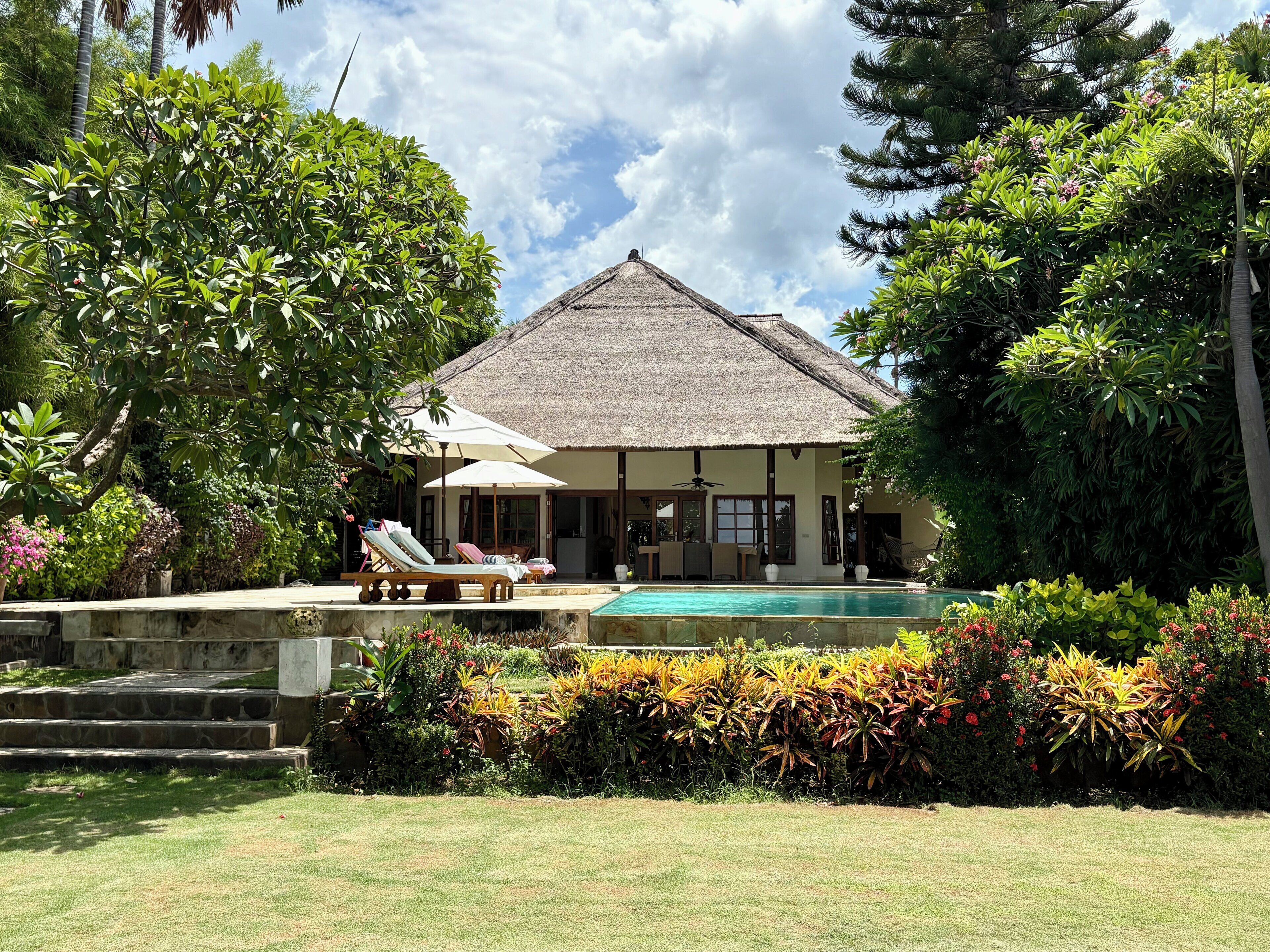 Ein Haus mit Pool, umgeben von üppiger Vegetation und einem Reetdach.
