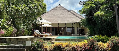 A house with a pool, surrounded by lush greenery and a thatched roof.