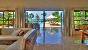 Ein geräumiges Zimmer mit großem Fenster, einer Couch und Blick auf Pool und Palmen.