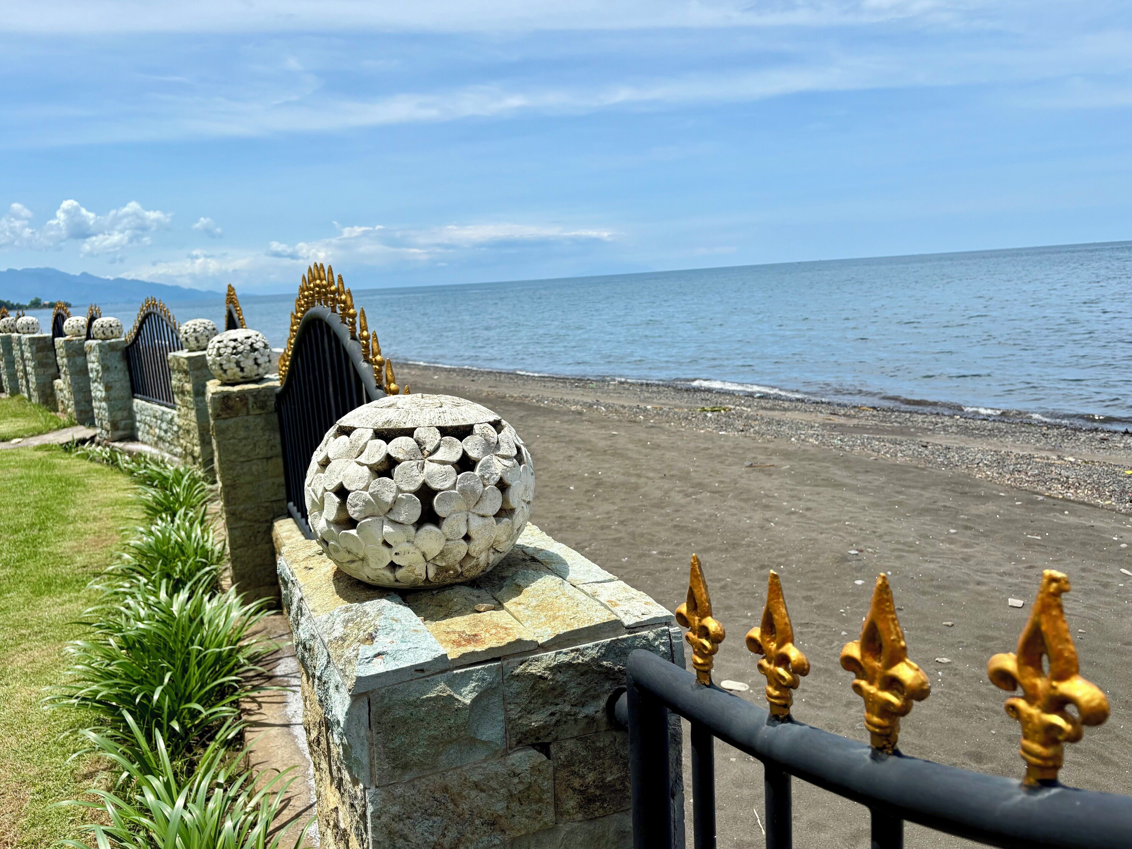 A coastal walkway with stone railings and decorative golden finials, leading to a beach.