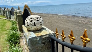 Ein Küstenweg mit Steinzaun und verzierten, goldenen Knäufen, der zu einem Strand führt.