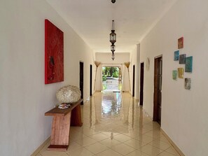 Un couloir avec un banc en bois, une œuvre d’art rouge et un luminaire au plafond.