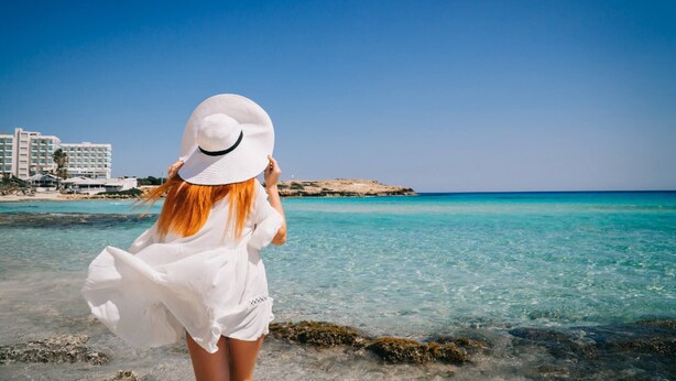 A person standing at the beach with a clear view of the sea and buildings in the background. - Napa Central Apartment (Ayia Napa)