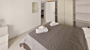A modern bedroom with a large bed, a wardrobe, a mirror, and a hanging light fixture. - Napa Central Apartment (Ayia Napa)