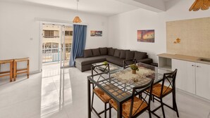 A modern living room with a glass dining table, a sofa, and a kitchen area. - Napa Central Apartment (Ayia Napa)