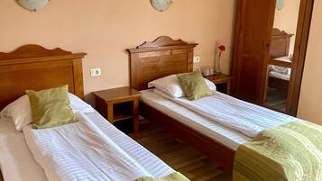 A room with two single beds, wooden headboards, a nightstand, a mirror, and a wall-mounted light fixture.