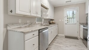 Una cocina con armarios blancos, encimera de mármol, lavavajillas y horno de acero inoxidable.