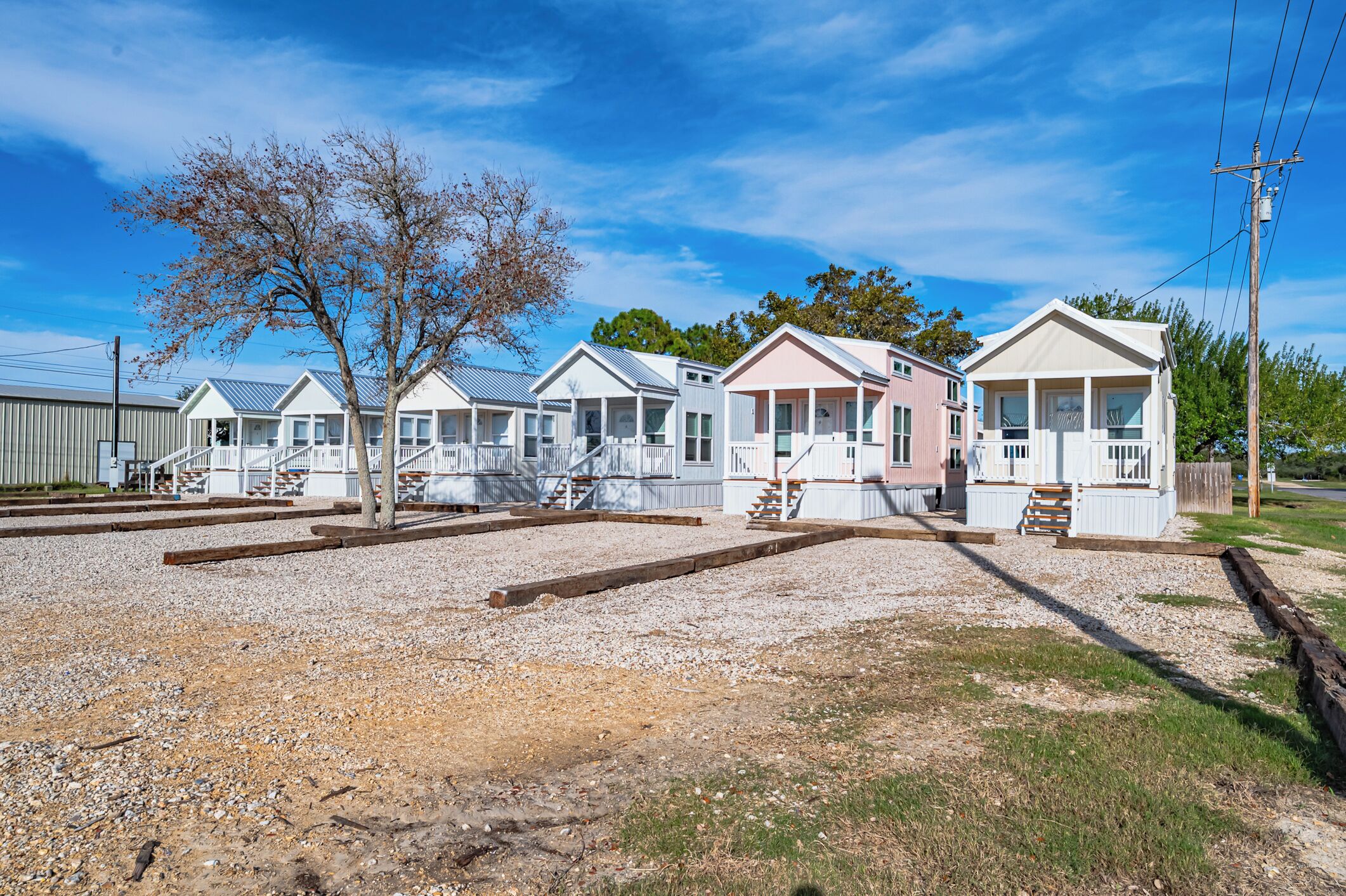 A row of mobile homes with a gravel driveway and a tree in the foreground.