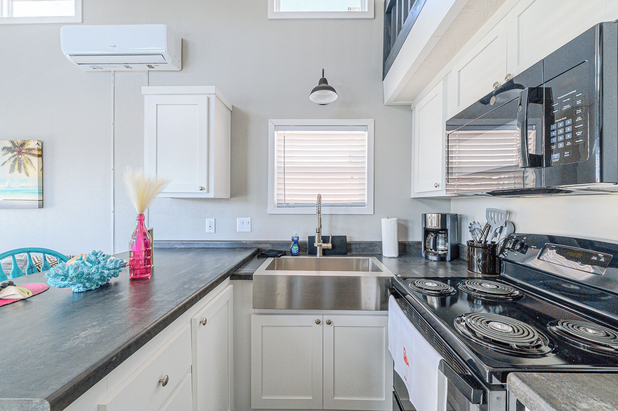 A modern kitchen with white cabinets, a stainless steel sink, a black stove, and a window with blinds.