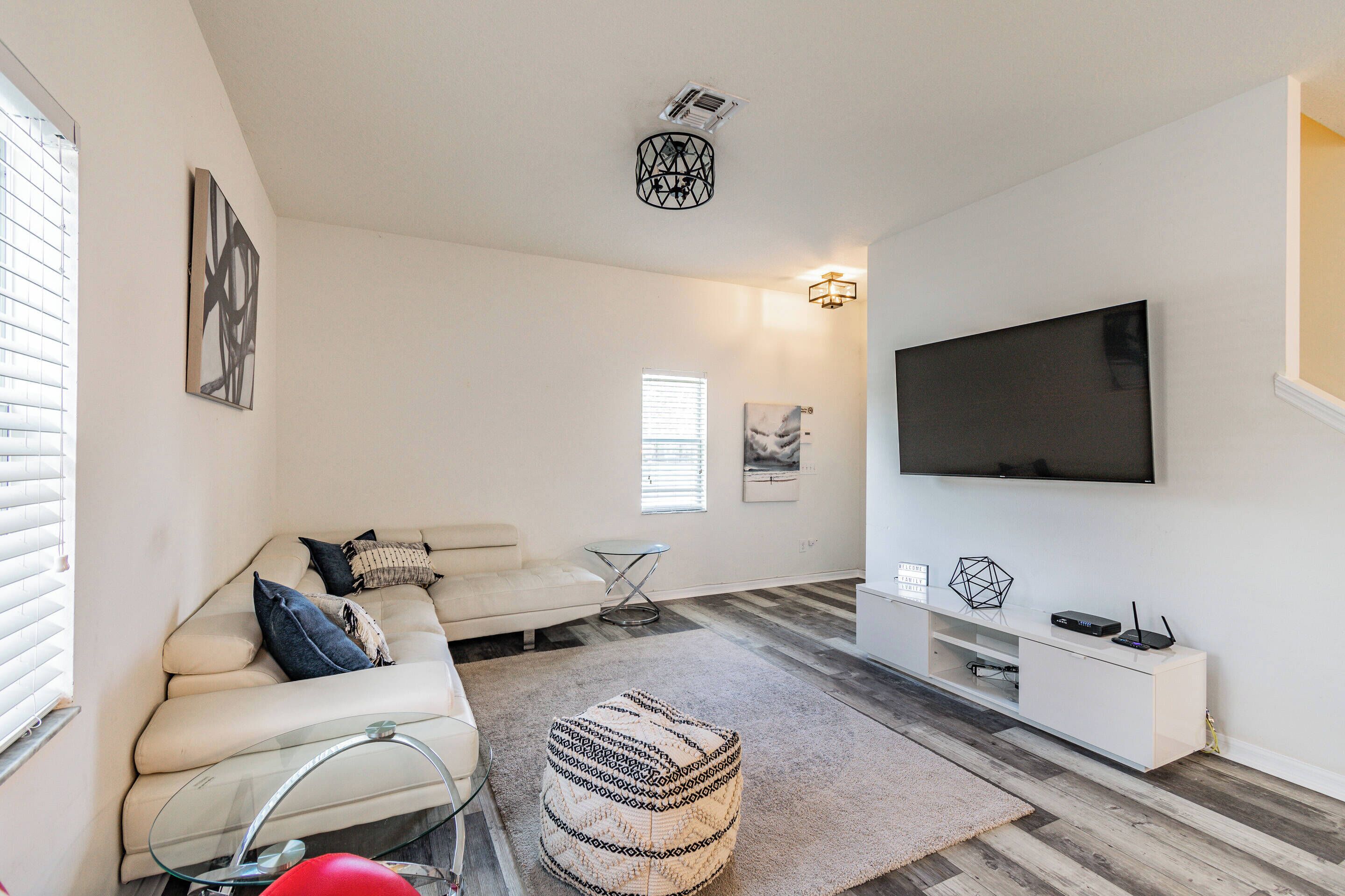 Een moderne woonkamer met een witte bank, poef en een tv-meubel met een flatscreen televisie.