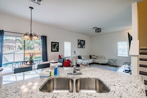 A modern kitchen with a double sink, dining area with a table and chairs, a red chair, and a white sofa. - 4BR Pool Home Near Disney Bella Vida (Kissimmee)