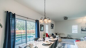Ein Essbereich mit großem Tisch, gedeckt für vier Personen, einer Hängeleuchte und Blick auf einen Swimmingpool durch große Fenster.