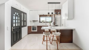 Una cocina moderna con armarios blancos, una isla central con taburetes y luces colgantes.