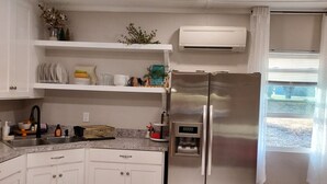 A kitchen with white cabinets, a stainless steel refrigerator, a built-in air conditioner, and a window with blinds. - Serene Modern Space on a Pecan Grove near Historic Downtown Abbeville (Abbeville)