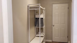 A hallway with a white metal shelving unit against the wall, a white door at the end, and wooden flooring. - Serene Modern Space on a Pecan Grove near Historic Downtown Abbeville (Abbeville)