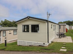 A single-story mobile home with two windows, a small porch, and a utility pole with wires. - Jurassic Discovery (Bridport)