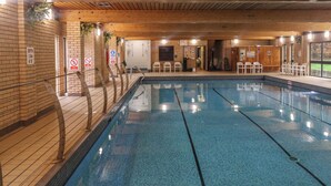 An indoor swimming pool with wooden beams on the ceiling, a tiled floor, and a brick wall. - Jurassic Discovery (Bridport)
