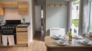 A modern kitchen with wooden cabinets, a stove, and a dining area set for four with white plates and wine glasses. - Jurassic Discovery (Bridport)