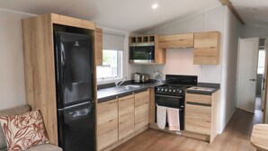 A compact kitchen with a refrigerator, stove, microwave, and wooden cabinets. - Jurassic Discovery (Bridport)