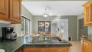 Una cocina con armarios de madera, encimera de granito, cafetera y un comedor con sillas y mesa.