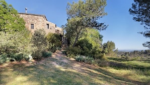 A stone building with a chimney, surrounded by trees and a grassy path. - Holiday Home 'Cal Malla Petit' with Mountain Views, Private Pool & Wi-Fi (Artes)