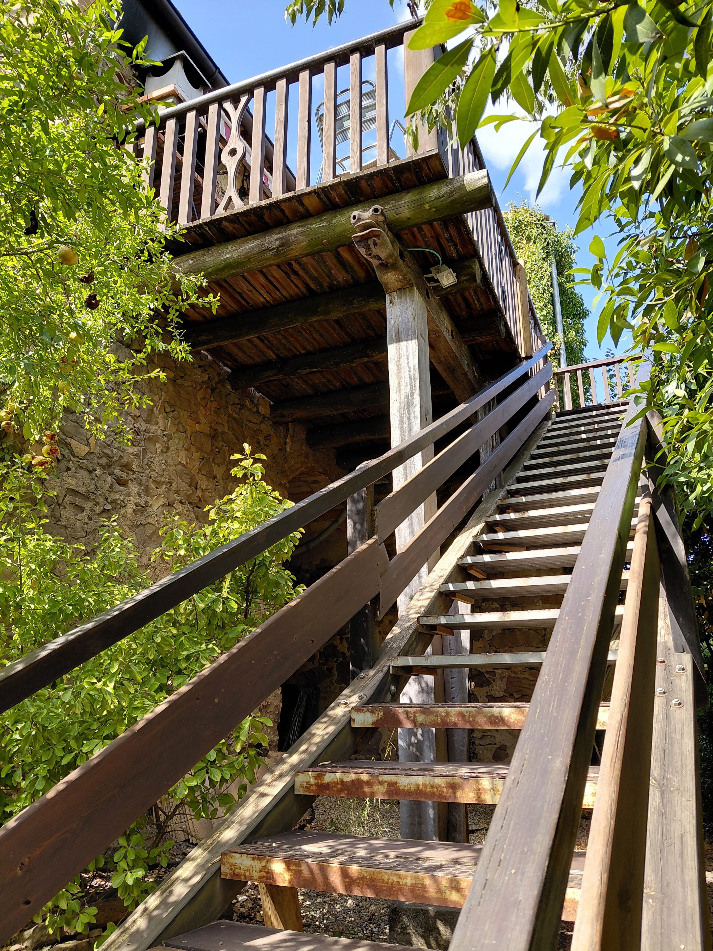 A wooden staircase leading up to a balcony with a stone wall backdrop.
