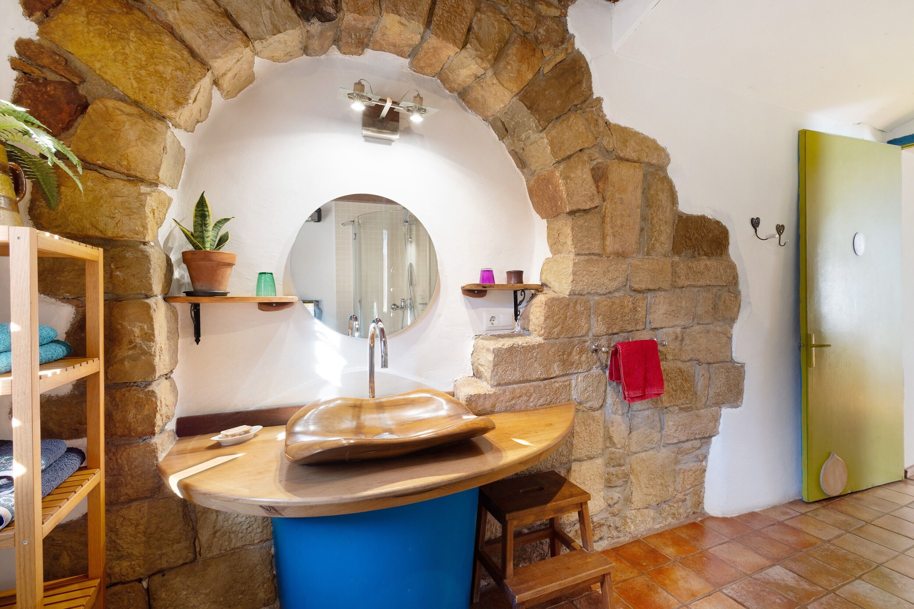 Un baño con un arco de piedra, un tocador de madera, un espejo y una puerta verde.