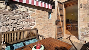 A stone building with a wooden bench and table, a red and white striped awning, and a door leading to an interior space. - Holiday Home 'Cal Malla Petit' with Mountain Views, Private Pool & Wi-Fi (Artes)