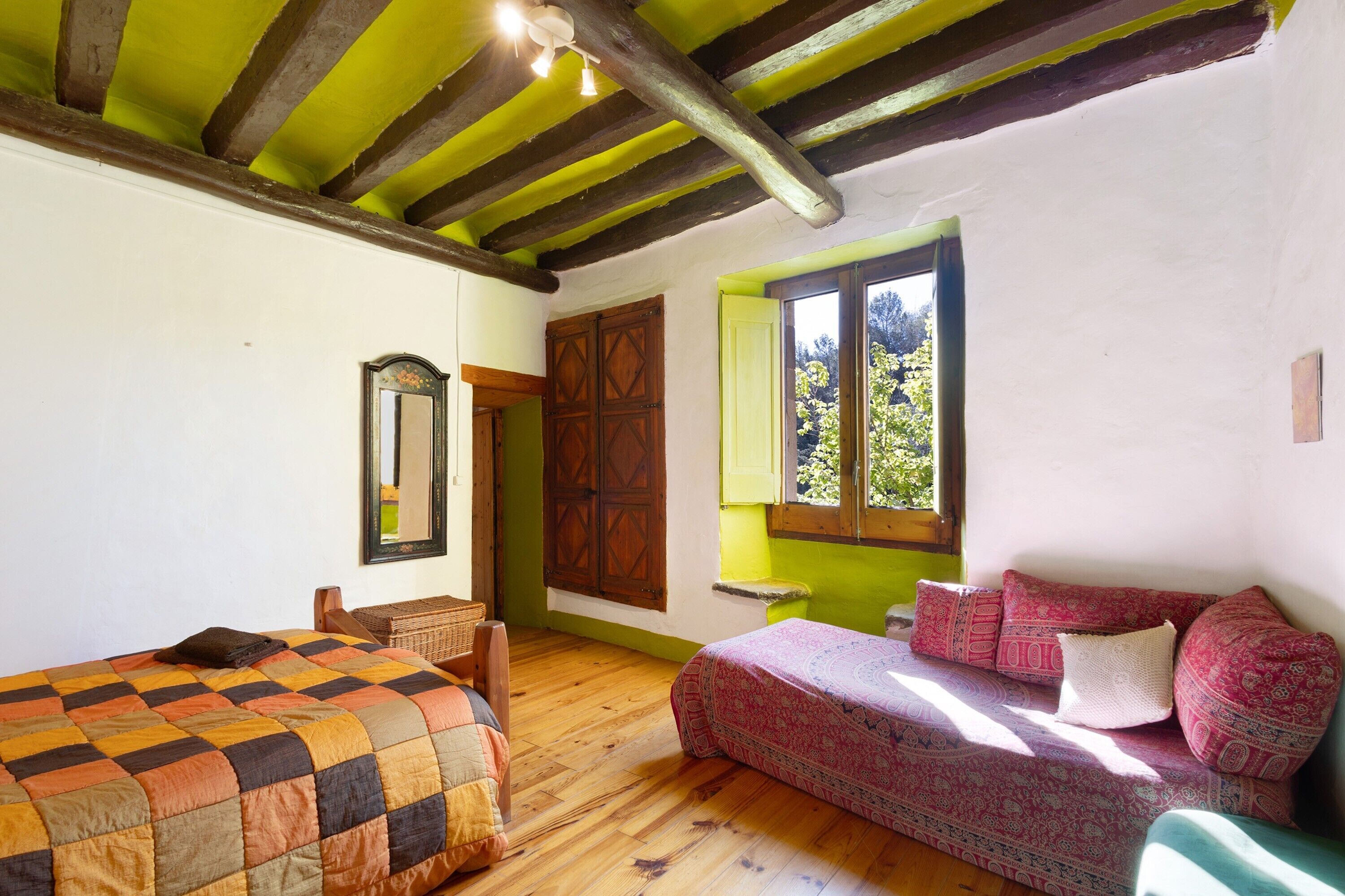 Una habitación con cama, sofá, espejo y ventana con vista a follaje.
