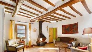 A cozy living room with a fireplace, wooden beams, a sofa, and a coffee table. - Holiday Home 'Cal Malla Petit' with Mountain Views, Private Pool & Wi-Fi (Artes)