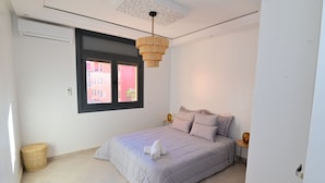 Ein Schlafzimmer mit Bett, Fenster, Deckenleuchte und einem kleinen Tisch mit Lampe.