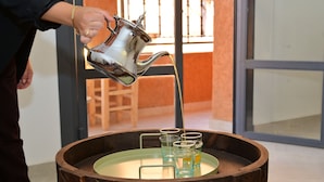 Eine Person gießt Flüssigkeit aus einem Metallkrug in eine Holzschale mit vier Gläsern.