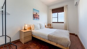 A bedroom with a bed, bedside tables, a lamp, a chair, a window with curtains, and a painting on the wall. - T3 Acolhedor perto da Universidade by LovelyStay (Faro)