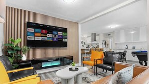 A modern living room with a flat-screen TV mounted on a wooden wall, a fireplace, and a seating area with a sofa and chairs. - The Big Group Paradise: Pool, Games, & More! (North Las Vegas)