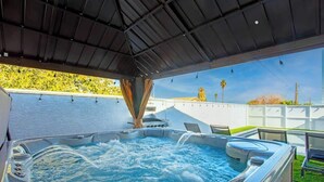 A hot tub with a metal roof, surrounded by a patio area with chairs and a view of a building with a yellow roof. - The Big Group Paradise: Pool, Games, & More! (North Las Vegas)